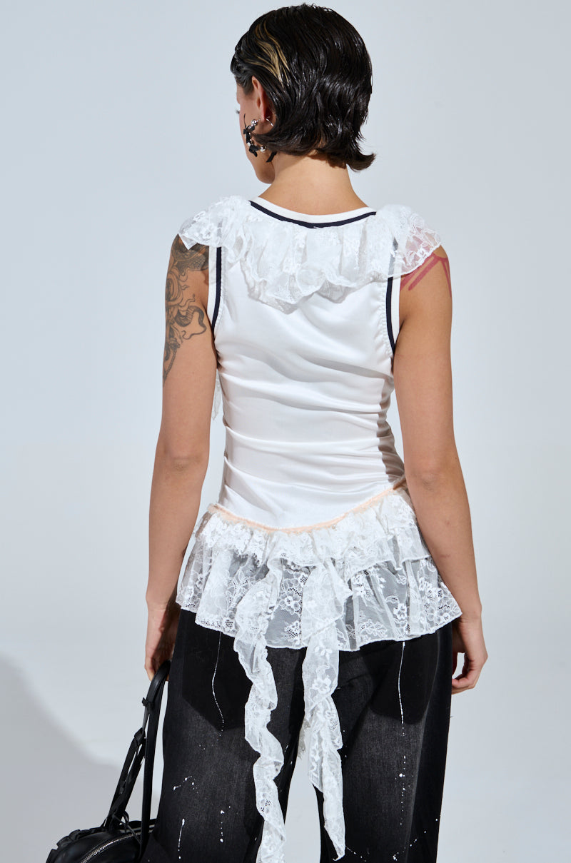 Someone with short hair radiates a sporty-chic vibe in the PLAY WITH MY HEART RUFFLE JERSEY and black pants with white streaks. Tattoos decorate their arm as they hold a stretchy black bag, turning away from the camera.