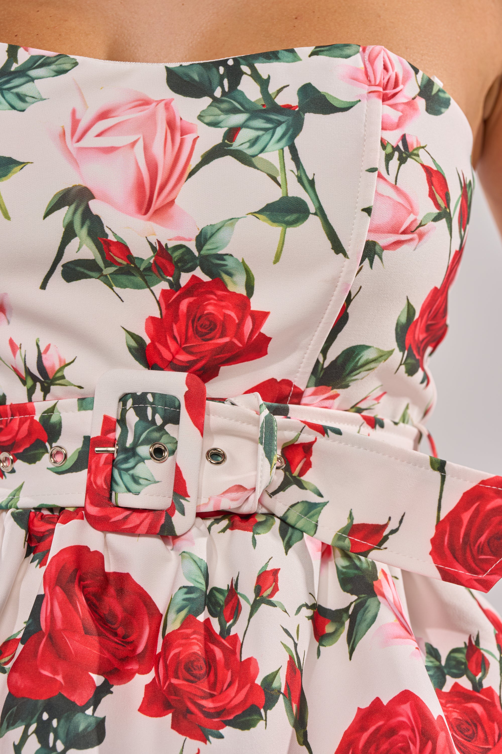 Close-up of the FULL BLOOM FLORAL CORSET, a strapless dress with red and pink rose prints, green leaves, a matching fabric belt with buckle at the waist, and a flattering corset-style bodice. 9