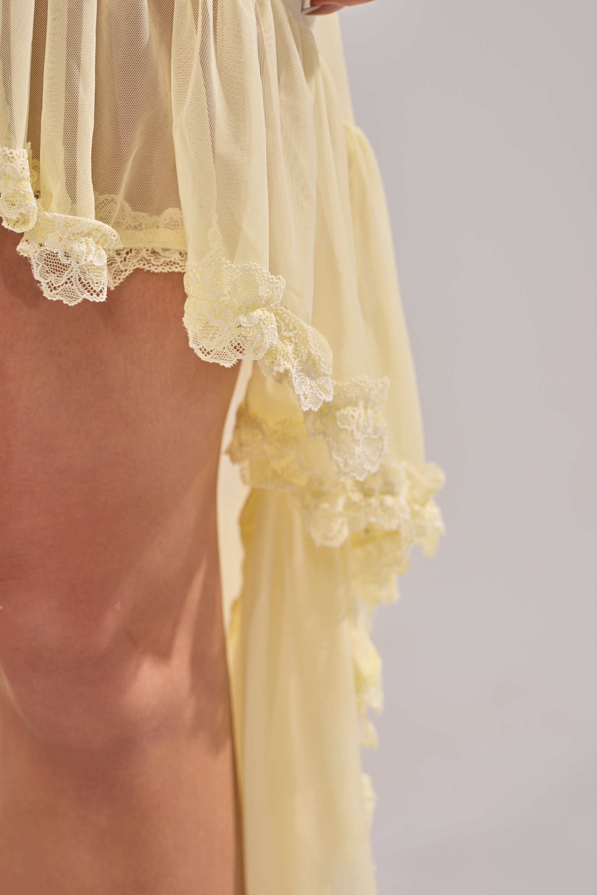 A close-up shows someone in the VACA VIBES MESH HIGH LOW SKIRT—a sheer mesh skirt with lace trim and a high-low hem—revealing part of their upper thigh against a light background. 11