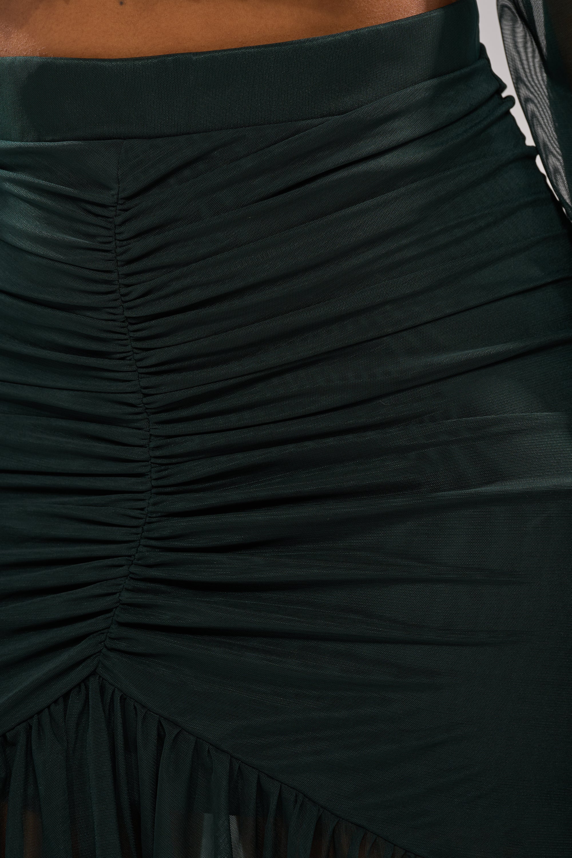Close-up of the EMERALD RUCHED HIGH LOW SKIRT—sheer mesh with gathered details and an asymmetrical hem—worn by a model. 5