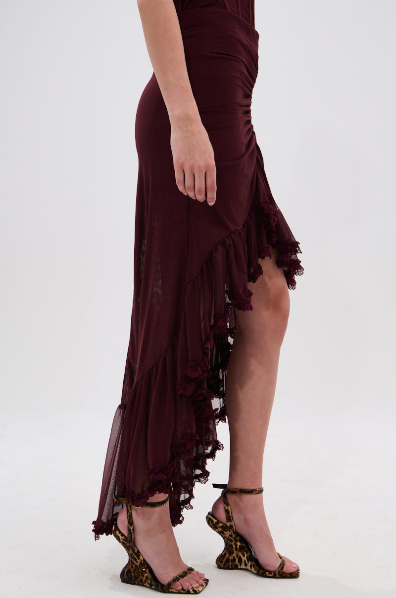 Wearing the LOVELY DAYS MESH HIGH LOW SKIRT in burgundy featuring an asymmetrical ruched design and paired with leopard-print heeled sandals, a person stands against a plain white background, showing only their lower half. 3