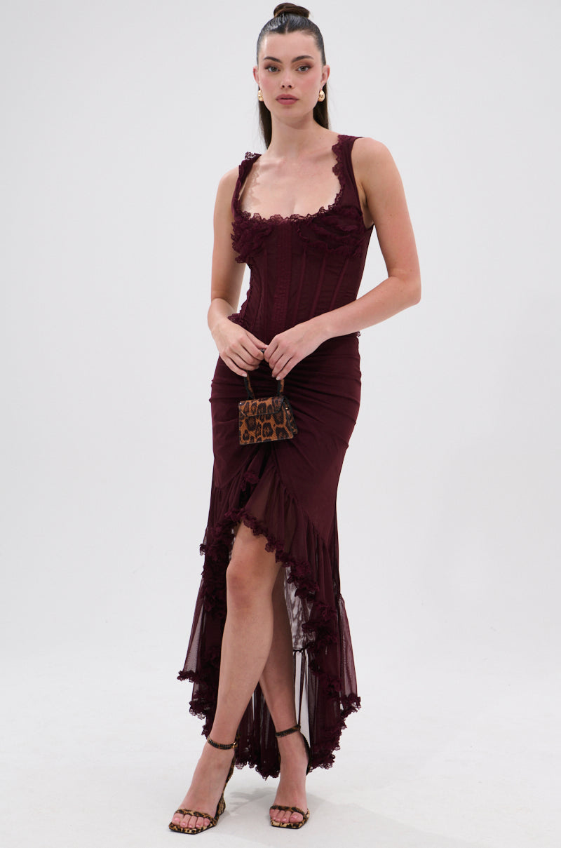 A woman stands against a white background wearing the LOVELY DAYS MESH HIGH LOW SKIRT in burgundy, paired with strappy heels and a leopard print purse. Her hair is styled in a sleek ponytail. 5