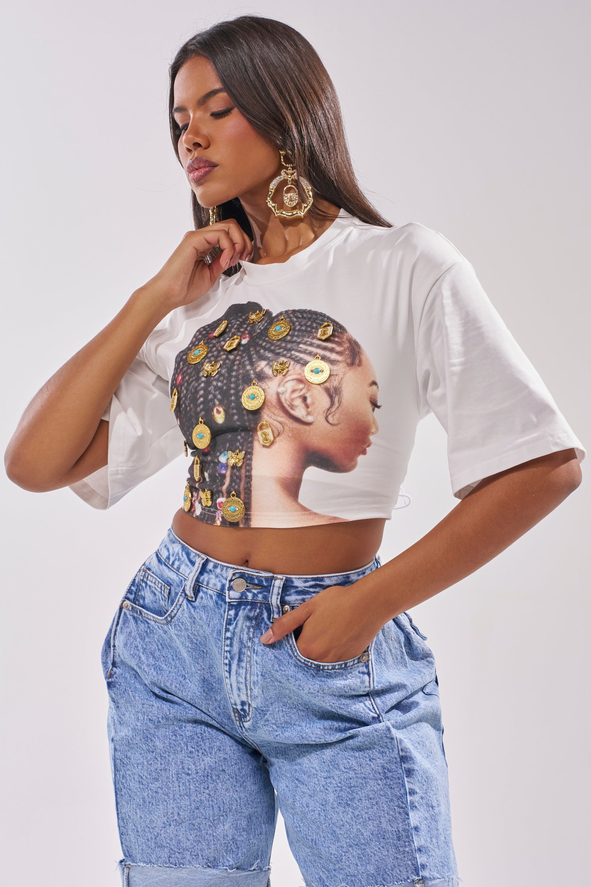 A woman wears the LOCKED AND LOADED EMBELLISHED TEE, featuring a side-profile graphic of a braided woman, paired with blue high-waisted jeans—an eye-catching look ideal for standout festival style. 2