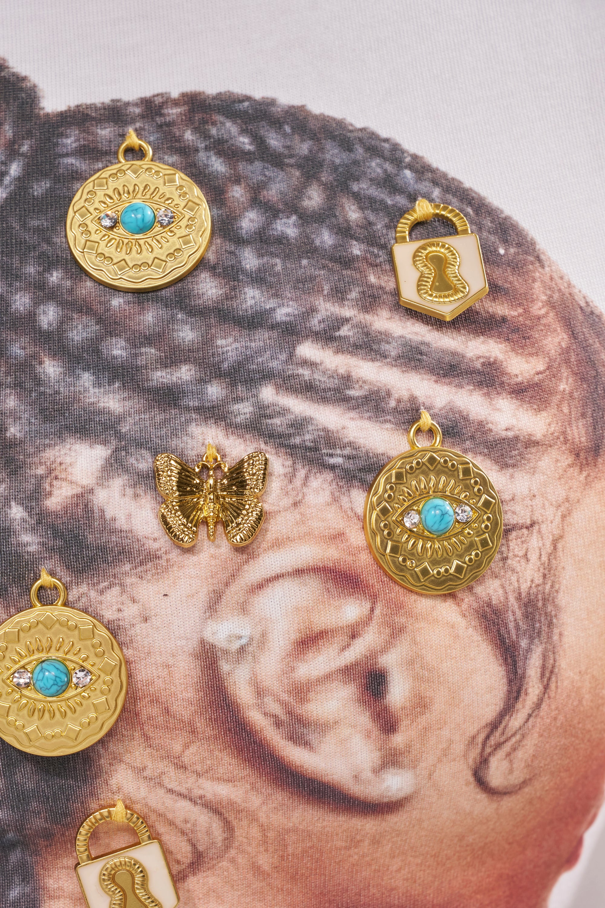 Close-up of the LOCKED AND LOADED EMBELLISHED TEE styled with a braided hairstyle and gold jewelry charms—featuring coins, turquoise stones, and butterflies—for festival-ready flair and a unique look. 7