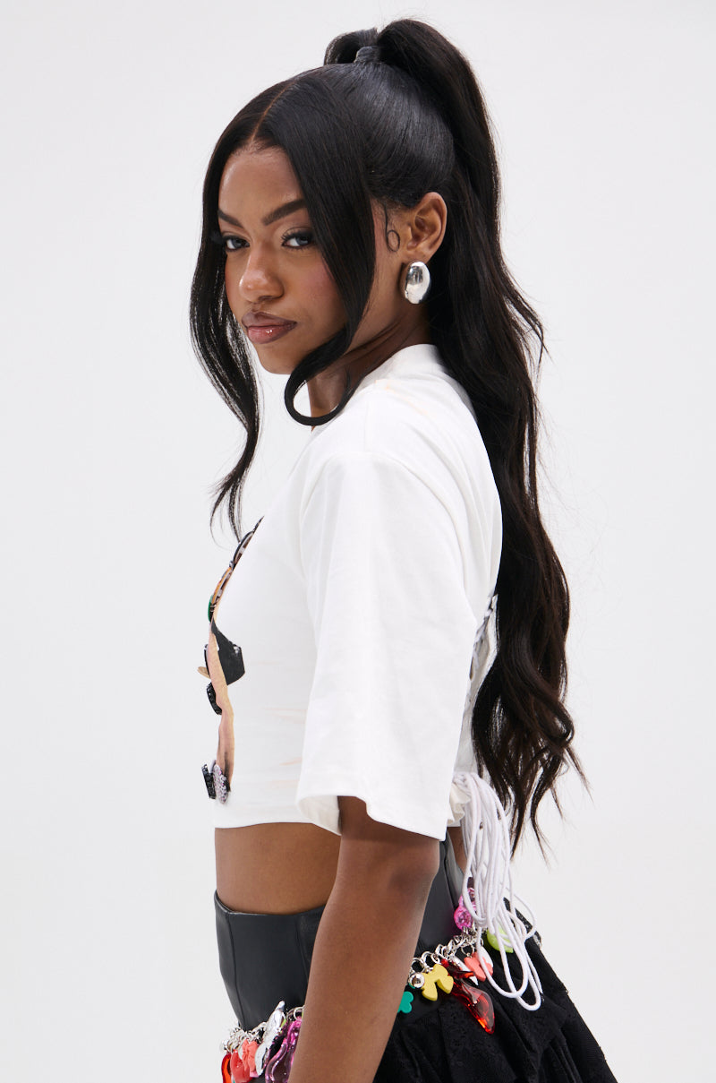 A woman with long, wavy black hair in a high ponytail wears the PIN IT TO WIN IT TEE, a black skirt with colorful accents, large hoop earrings, and looks confidently over her shoulder against a plain background.