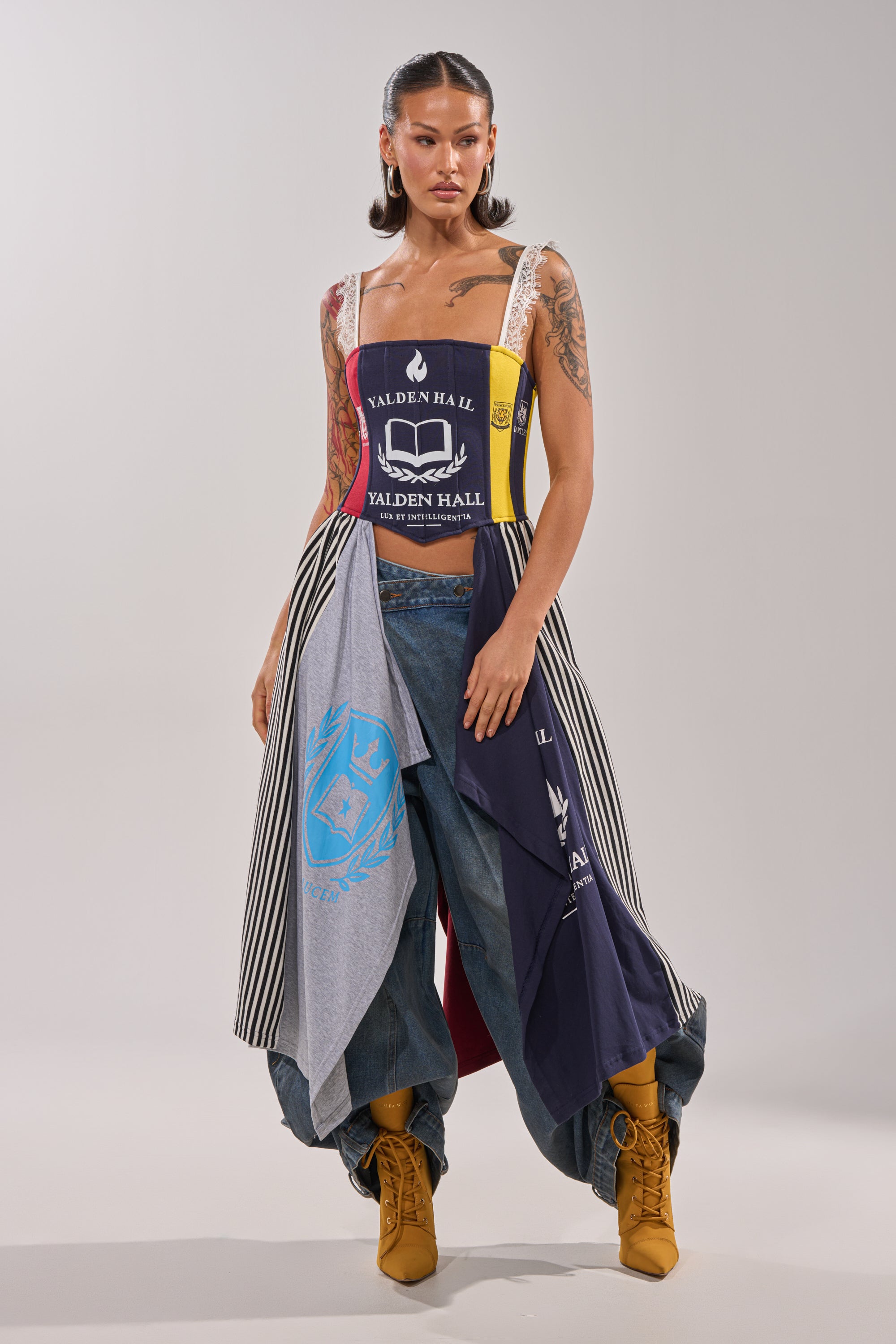 A woman stands confidently in the UNIVERSAL CORSET paired with wide printed pants, yellow lace-up boots, and bold earrings—creating a vibrant modern streetwear look against a plain background. 2