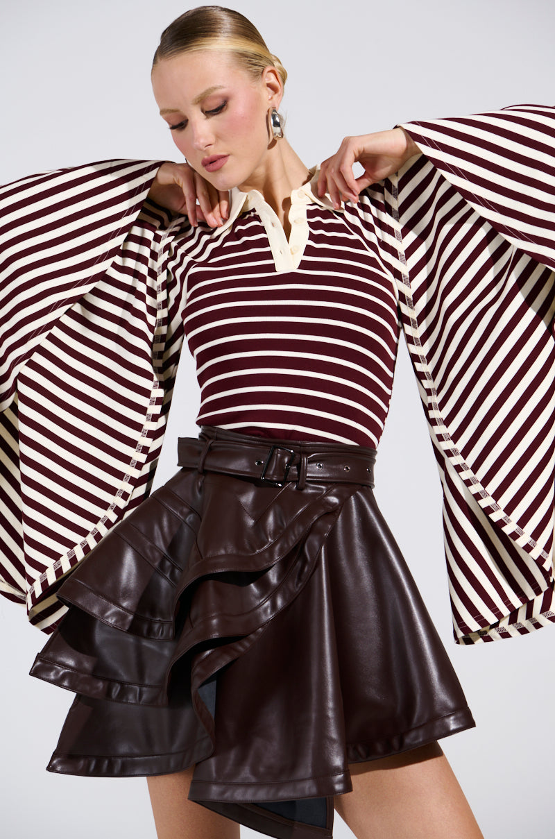 A woman channels retro style in the ALMA STRIPE COLLARED BODYSUIT paired with a dark brown ruffled leather mini skirt, silver earrings, and slicked-back hair.