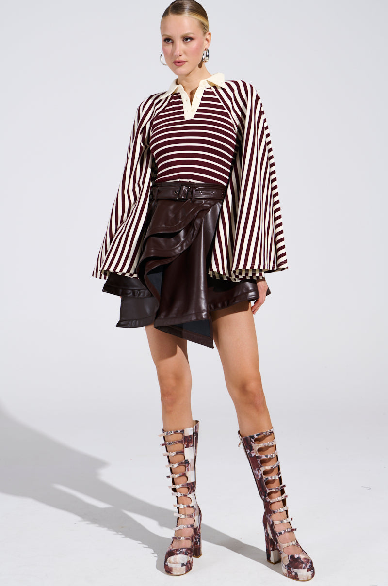 A woman poses in a stylish outfit featuring the ALMA STRIPE COLLARED BODYSUIT, paired with a dark brown leather mini skirt with ruffle details and knee-high, lace-up marbled boots.