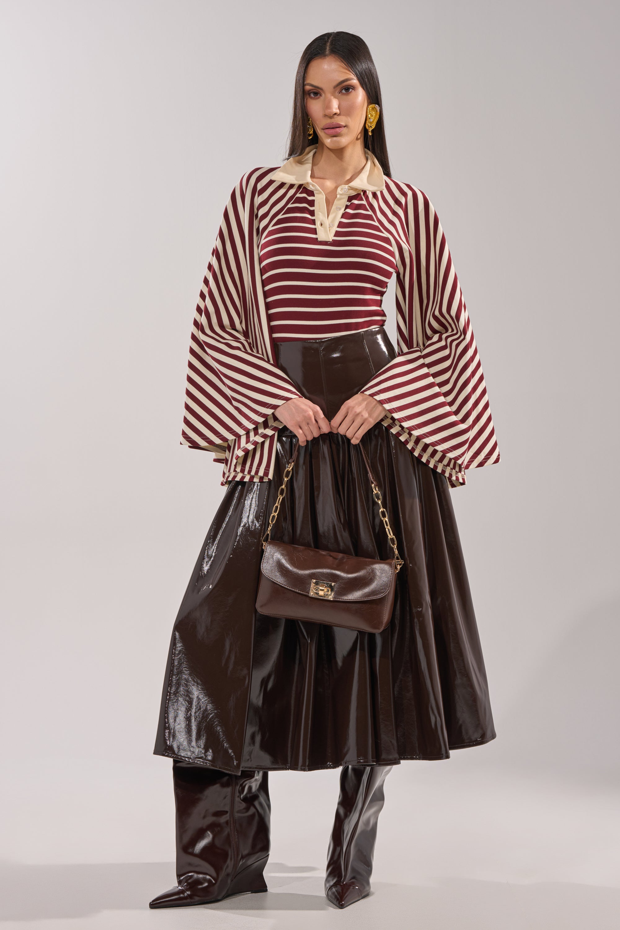 A woman poses in the ALMA STRIPE COLLARED BODYSUIT, styled with a dark brown midi skirt, matching over-the-knee boots, and a brown handbag with a gold chain strap against a plain background. 6