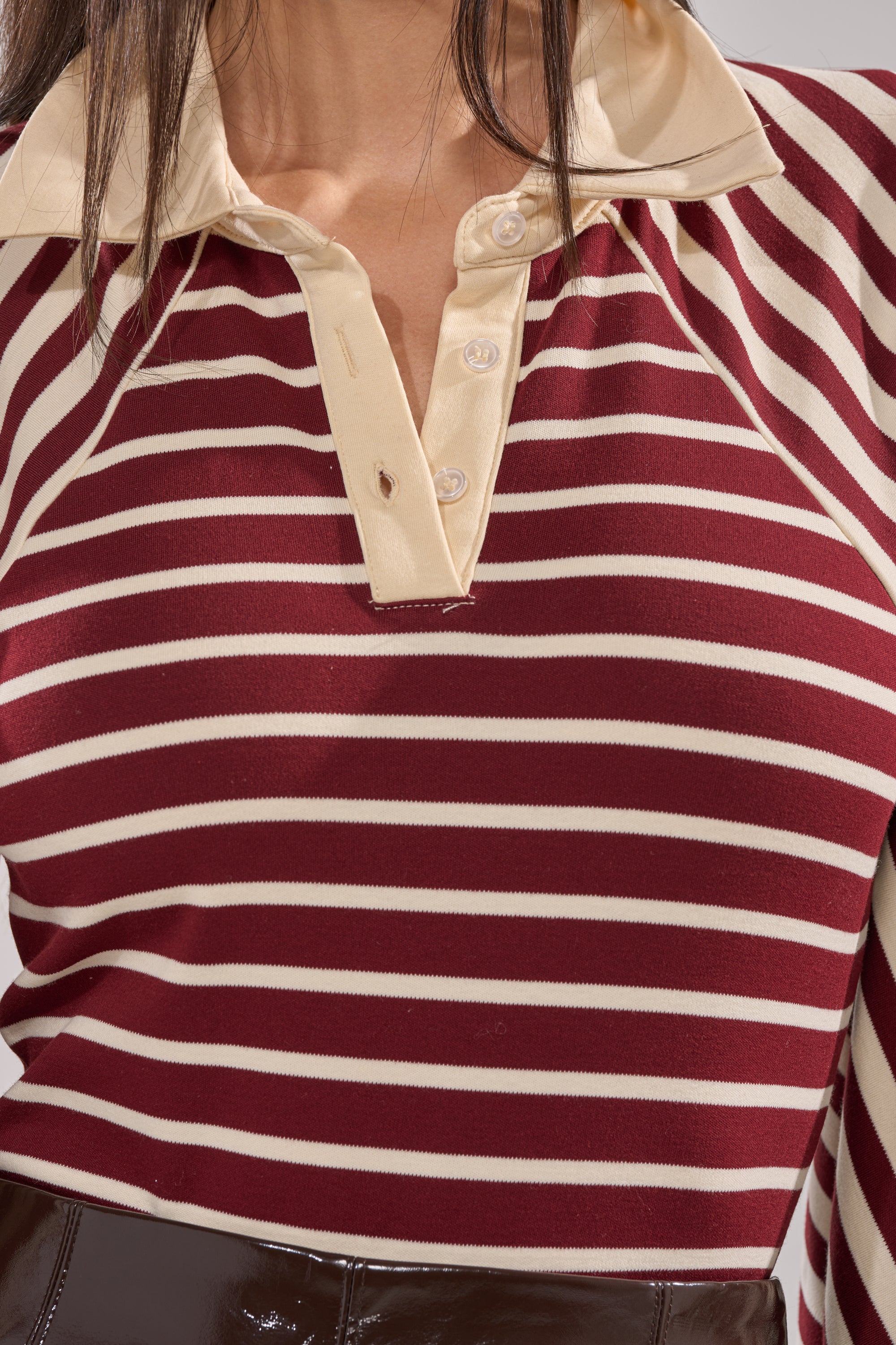 A person wears the ALMA STRIPE COLLARED BODYSUIT featuring maroon and white stripes, a beige collar, and a button placket. Only their torso and part of their hair are visible. 7