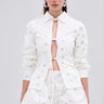 A woman models the LUX FASHION BLOUSE, a white cotton-blend shirt with metallic closures, paired with a floral sequin bubble skirt and hoop earrings, set against a light gray background.