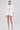 A woman with slicked-back hair and open-toed heels wears the LUX FASHION BLOUSE, a white cotton-blend button-up featuring cutouts and floral sequin details, paired with matching puffy shorts, set against a plain background.