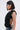 A woman with a sleek bob wears large hoop earrings, a chunky chain necklace, and the FOREVER AND EVER SLINKY TOP WITH LACE UP BACK, featuring ruched ruffle details, paired with light blue jeans. She is shown in profile against a plain background.