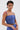 A person with short dark hair, white hoop earrings, and visible shoulder and chest tattoos models the BUSINESS ONLY BRALETTE—a blue and white striped tank crop top with buttons—against a plain white background.