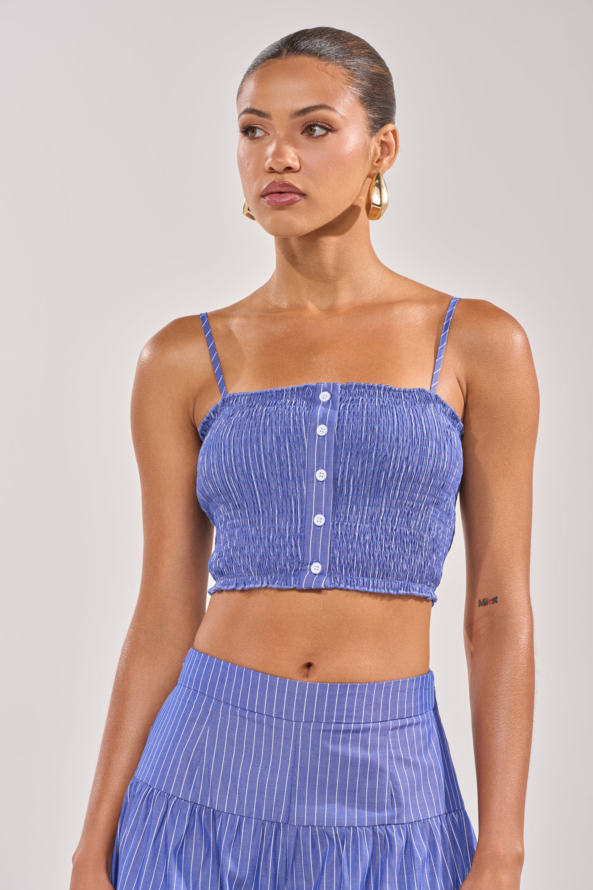 A woman wears the BUSINESS ONLY BRALETTE, styled with a matching pinstriped skirt and large hoop earrings. Her hair is pulled back as she poses against a neutral background, channeling a fresh nautical summer vibe.
