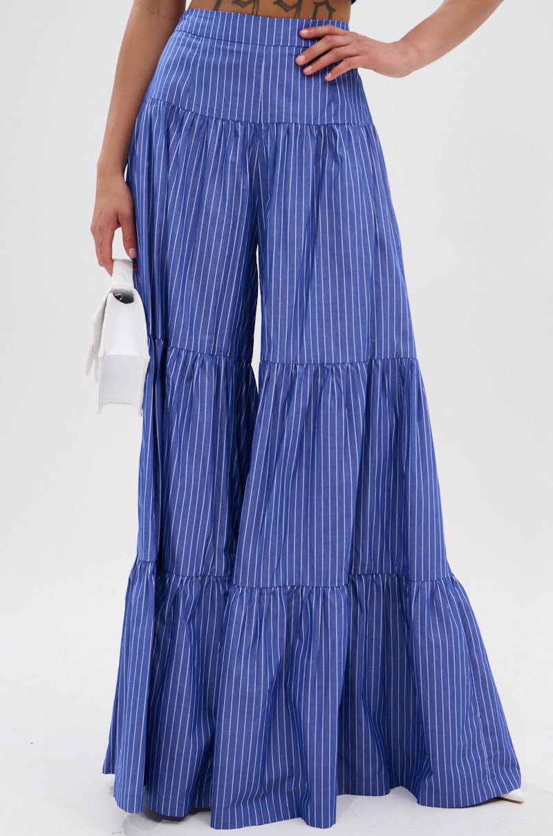 Wearing the BUSINESS ONLY STRIPE PALAZZO PANT, featuring a high-rise fit, wide-leg silhouette, and tiered ruffles, paired with a small white handbag.