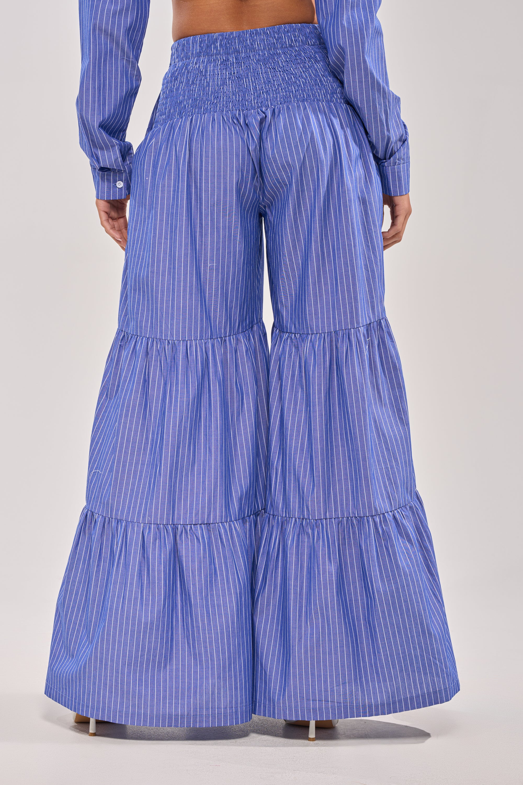 A person is shown from the back against a plain background wearing the BUSINESS ONLY STRIPE PALAZZO PANT, a blue striped high-rise, wide-leg pant, paired with a matching long-sleeve top.