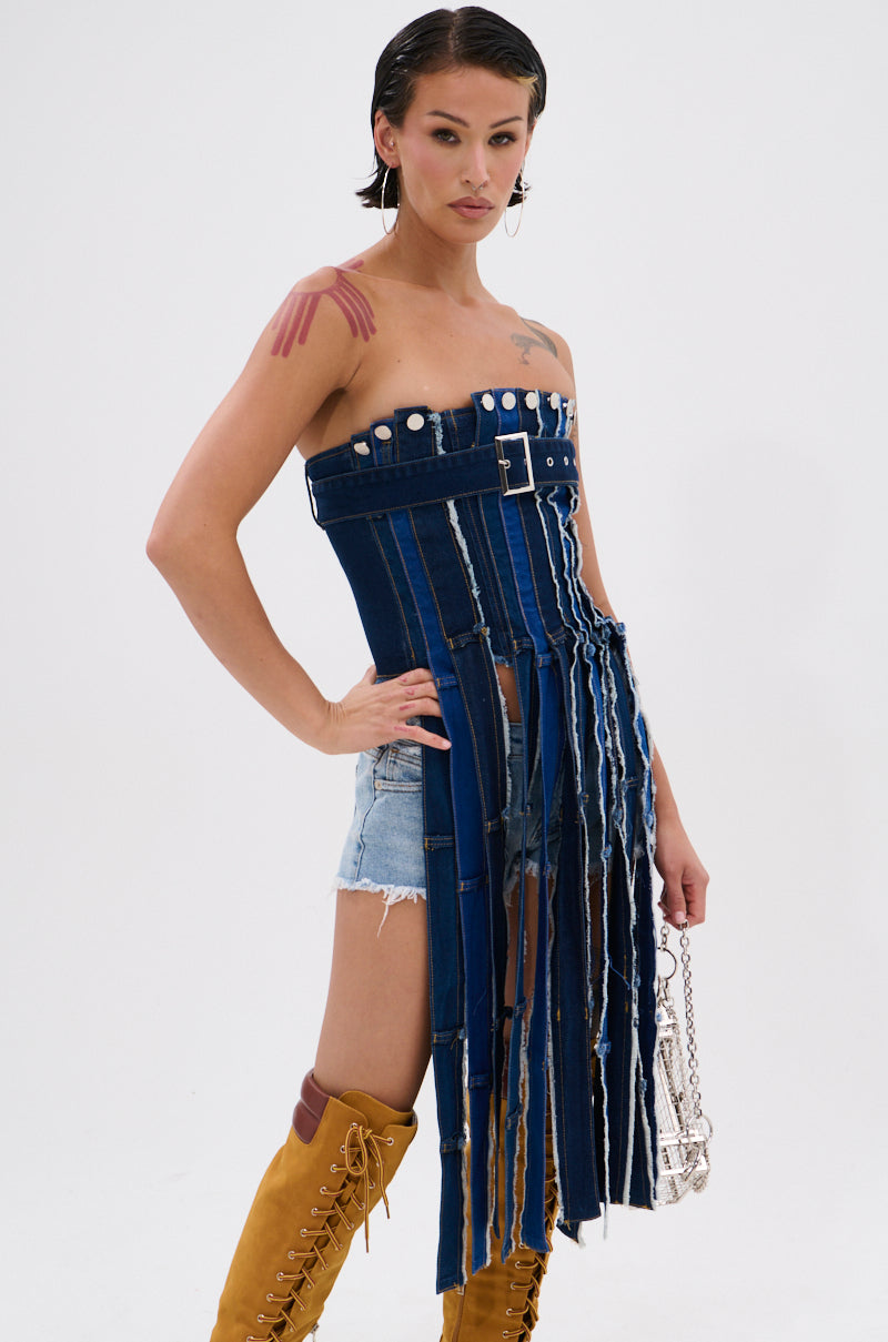 A person with wet, slicked-back hair models the GOT A LOT GOING ON DENIM CORSET—a strapless top with long vertical fringe—paired with denim shorts, tan lace-up boots, and a silver chain bag against a plain white background. 2