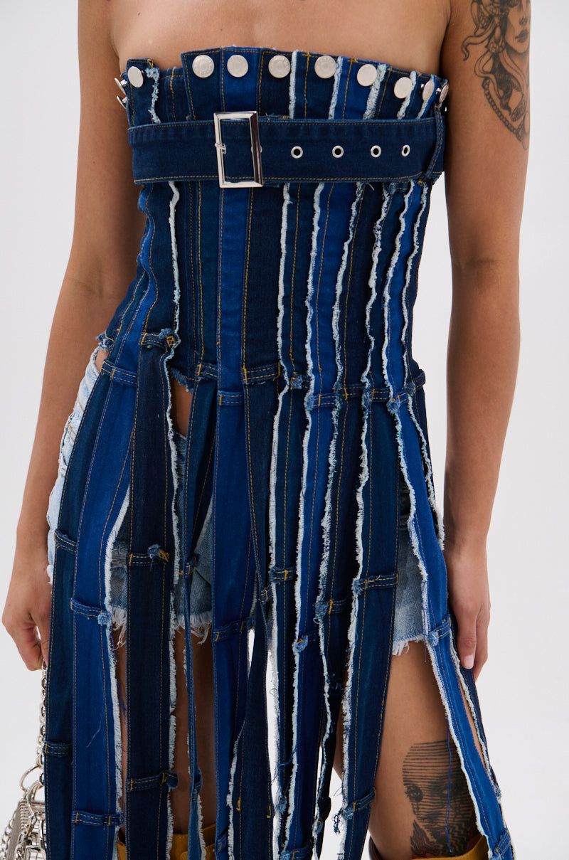 Wearing the GOT A LOT GOING ON DENIM CORSET, featuring frayed strips in varied blue shades, a belt, and metal studs, paired with distressed denim shorts for a bold, upcycled look that shows off tattooed arms. 7