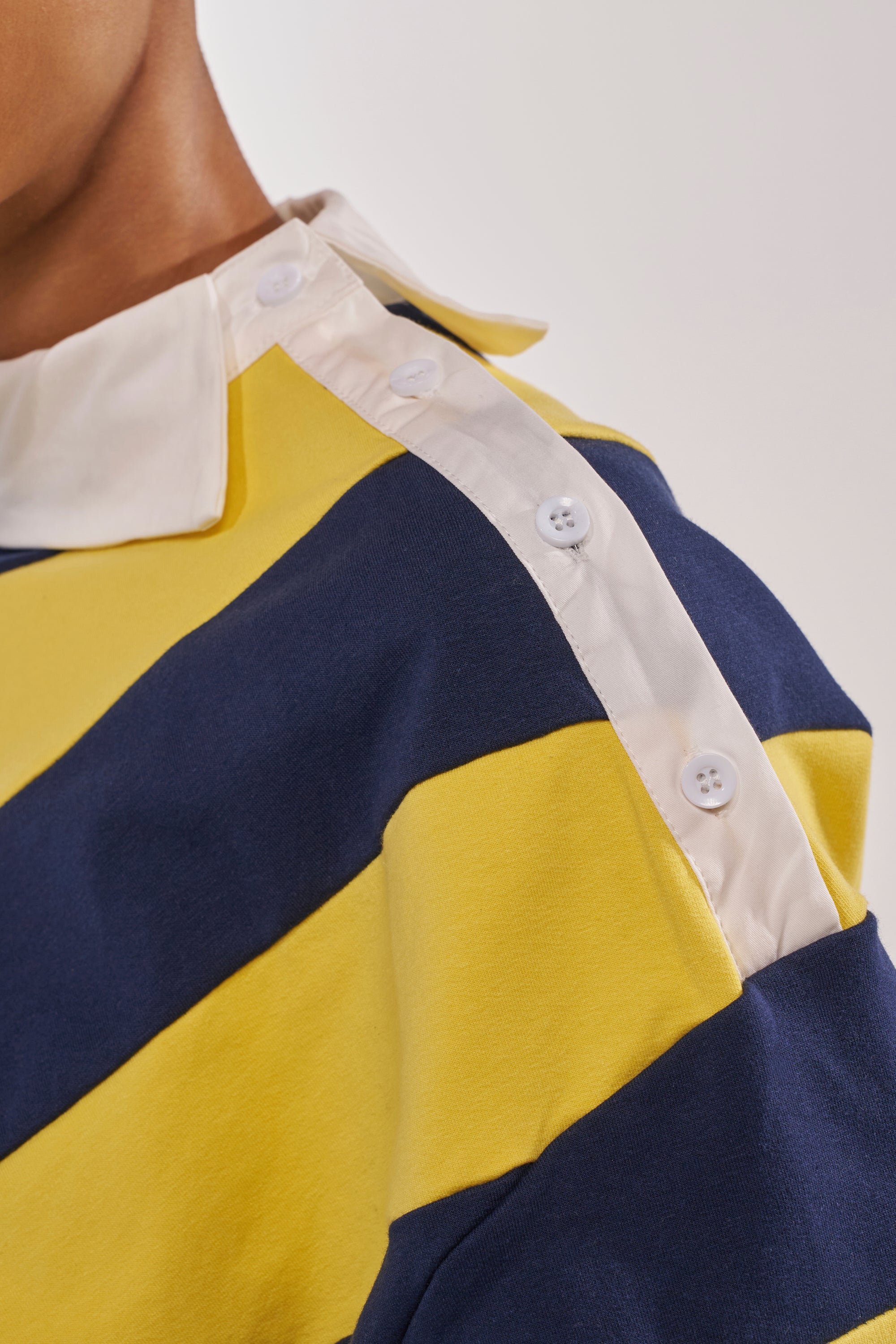 Close-up of a person wearing the JULIANA STRIPE SWEATSHIRT IN YELLOW, a cotton striped shirt with navy and yellow stripes, white collar, and three-button shoulder placket, shown against a neutral background. 5