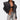 A woman with torso tattoos and slicked-back hair poses confidently in the COSMO ZIPPER MOTO jacket, black bra, ripped light-wash jeans, sunglasses, and a small handbag.
