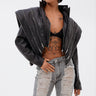 A woman with torso tattoos and slicked-back hair poses confidently in the COSMO ZIPPER MOTO jacket, black bra, ripped light-wash jeans, sunglasses, and a small handbag.