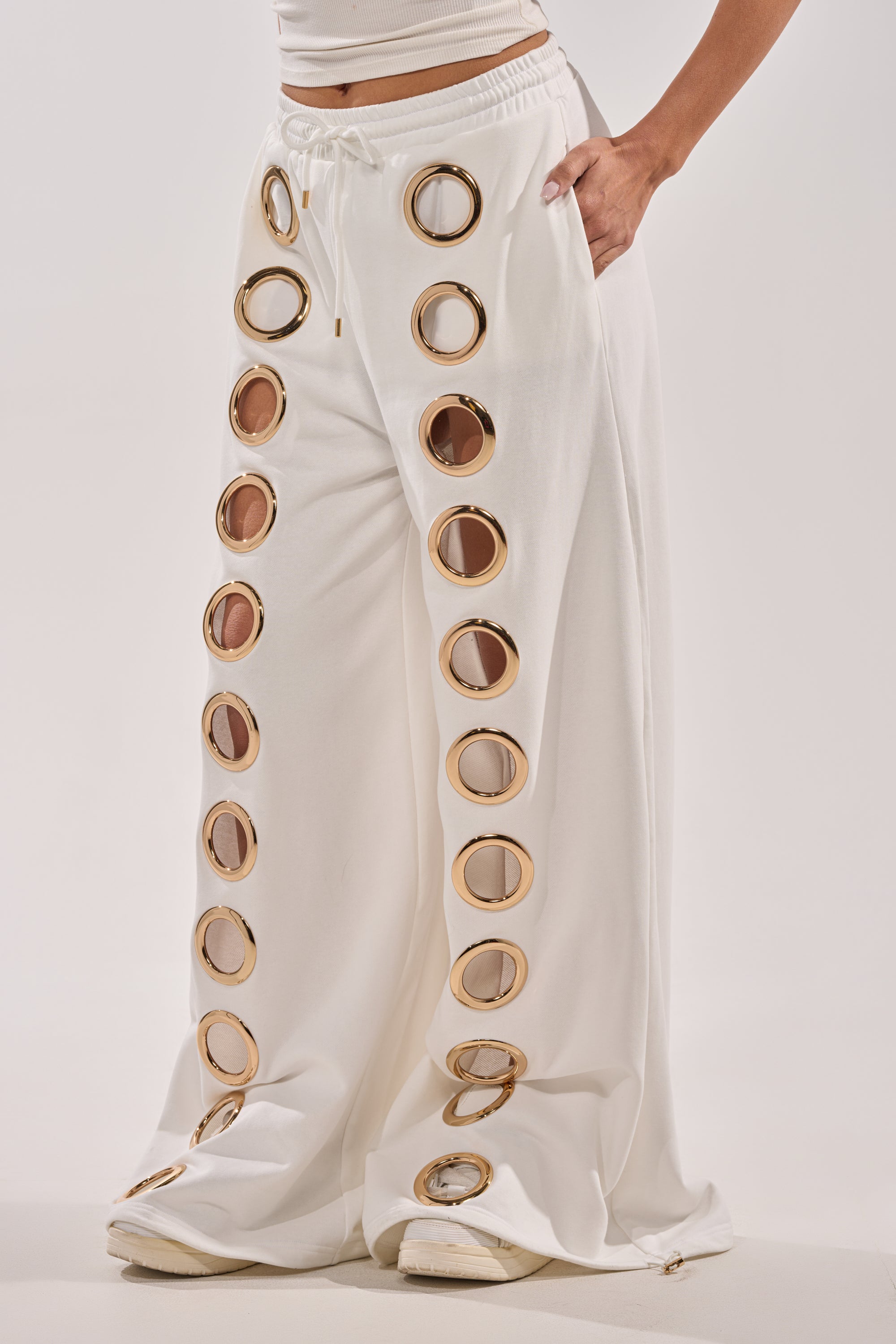 Wearing the THROUGH THE NIGHT WIDE LEG SWEATPANT WITH HOLES IN WHITE, featuring bold front cutouts, this look pairs white shoes and a hand-in-pocket pose for a striking athleisure statement. 3