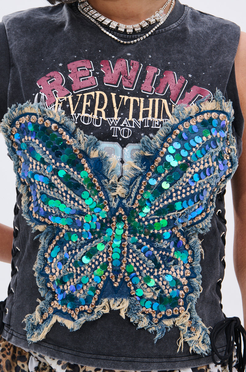 Wearing the REWIND EVERYTHING TEE with neon "BE WILD" text and a bold 3D blue-green sequin butterfly patch on distressed fabric, styled with a jeweled necklace for an edgy vibe.