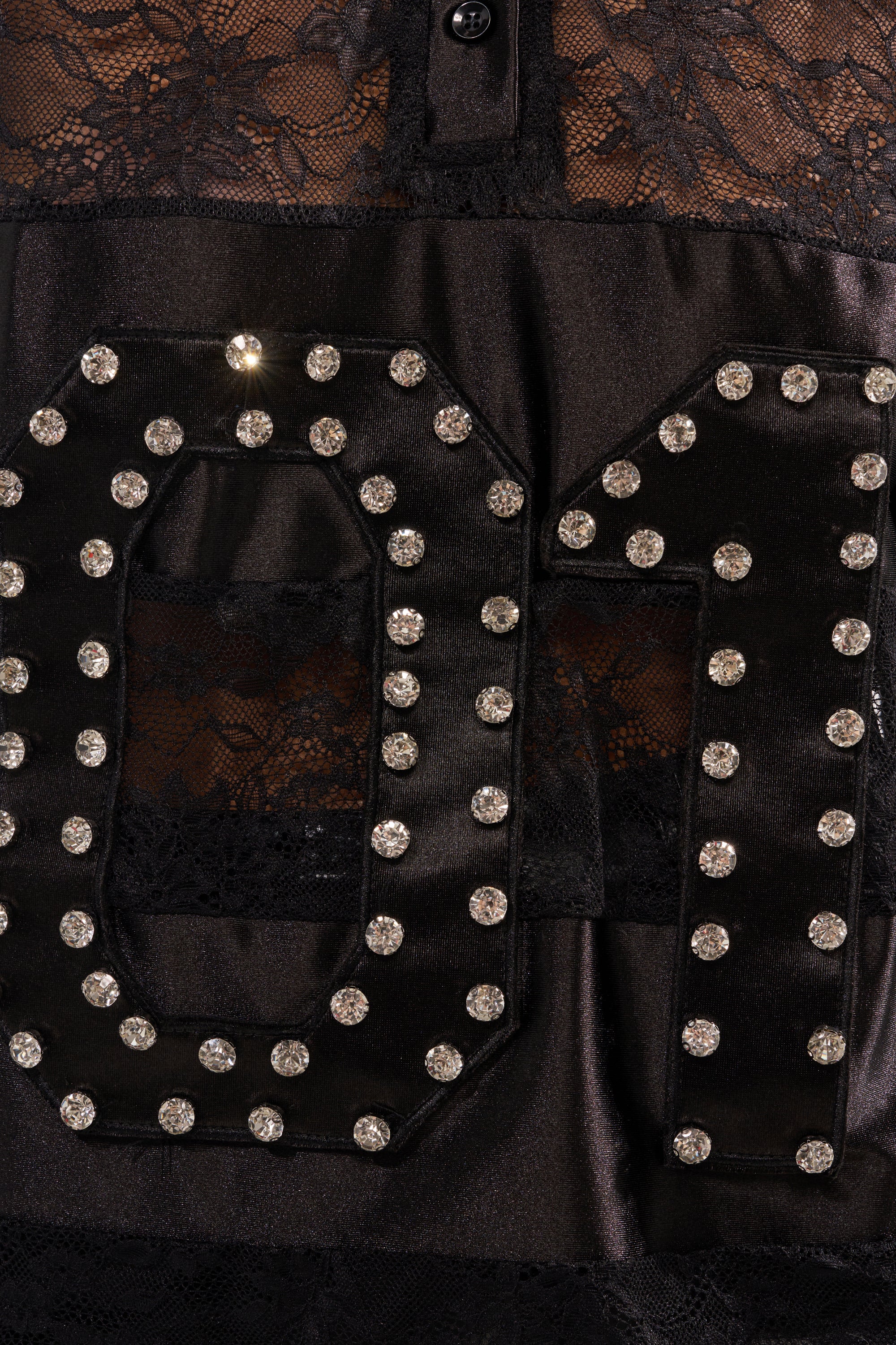 Close-up of the AT THE GAME PU LACE JERSEY TOP: black lace with large, shiny rhinestone "O" and "M" letters over a sheer floral background and glossy fabric, finished with decorative top buttons for an elegant touch. 6