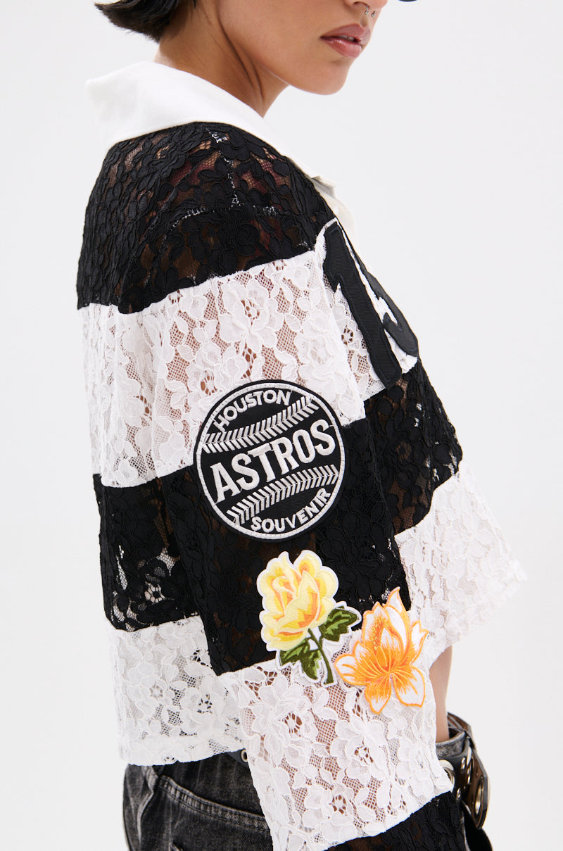 A person wears the GIVE ME TIME LACE JERSEY, a varsity-inspired black and white jacket with yellow flower appliqués and a round "Houston Astros Souvenir" patch, standing against a plain white background. 9