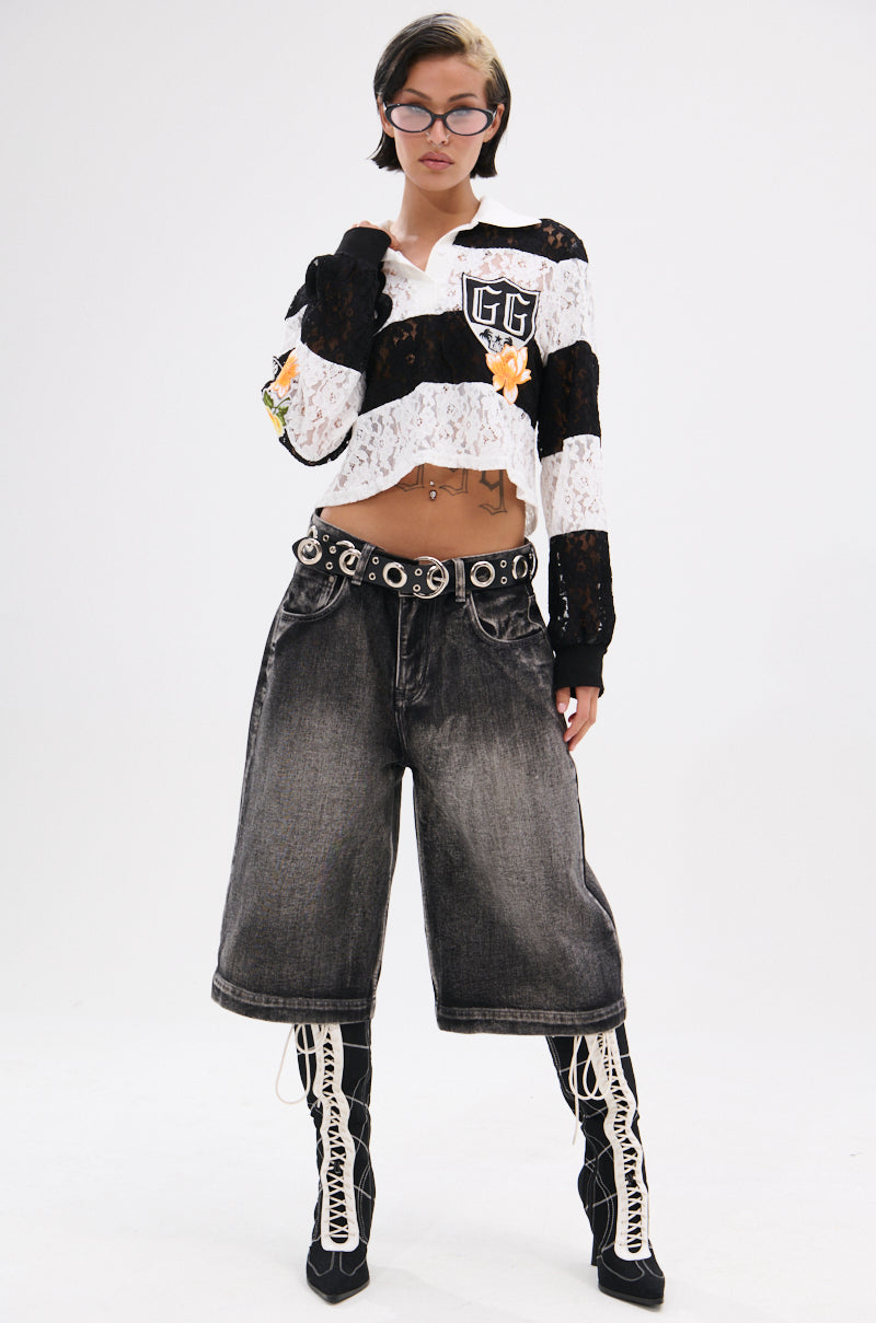 Wearing the GIVE ME TIME LACE JERSEY crop top with loose black denim shorts, knee-high lace-up boots, a grommet belt, and glasses, a person with short hair poses confidently against a plain background. 8