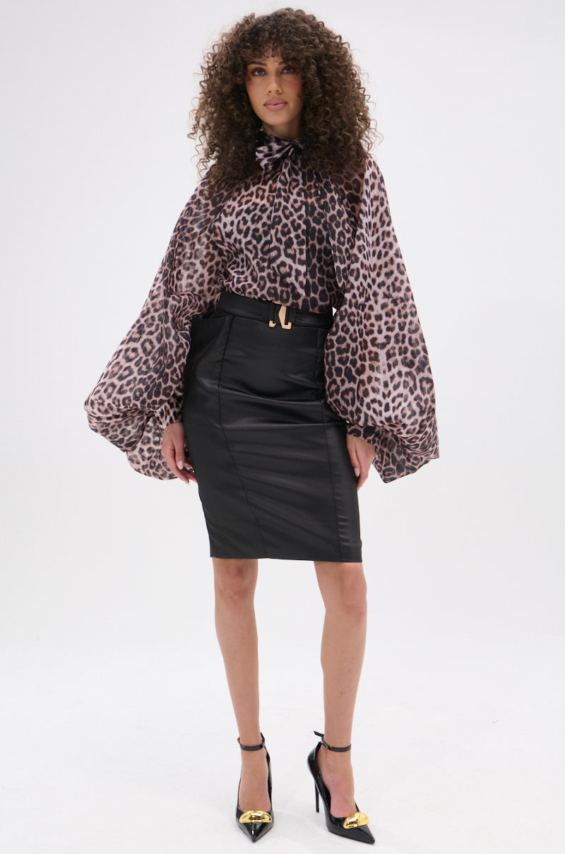 A woman with curly hair models the ROXY CHEETAH BLOUSE featuring voluminous sleeves, styled with a black knee-length leather skirt, gold belt accent, and black heels with gold pointed toes, against a plain white background.