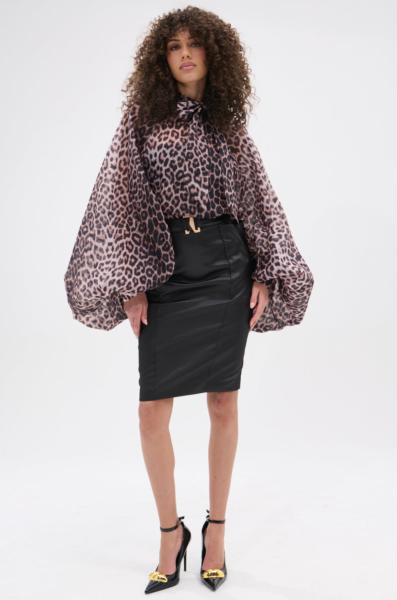 A woman with curly hair models the ROXY CHEETAH BLOUSE—sheer chiffon with wide, billowy sleeves—paired with a black knee-length pencil skirt and black heels with gold accents against a plain white background.