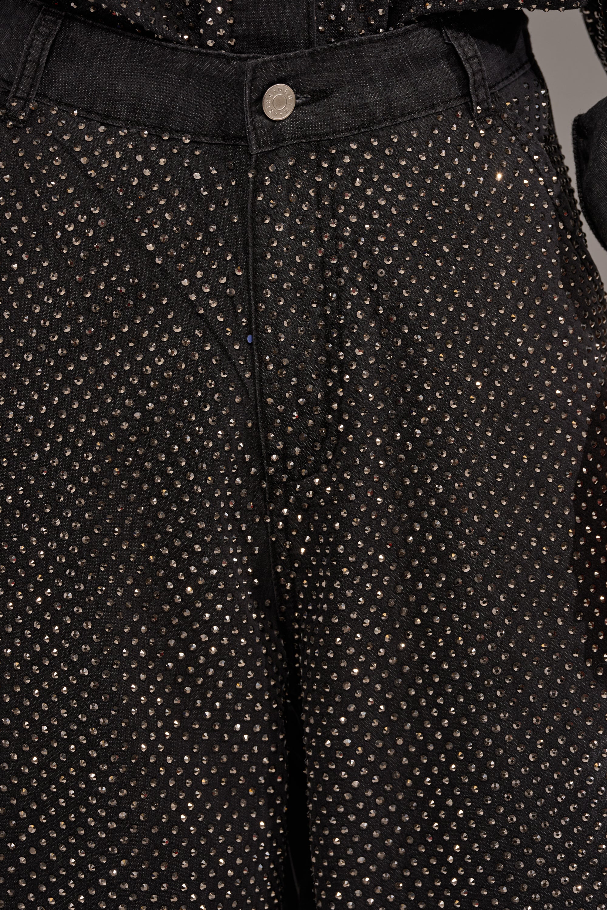 Close-up of the BLING BLING DENIM RELAXED PANT IN BLACK—wide-leg black denim pants adorned with small, shiny rhinestones and a visible button and waistband, perfect for adding sparkle to your style. 8
