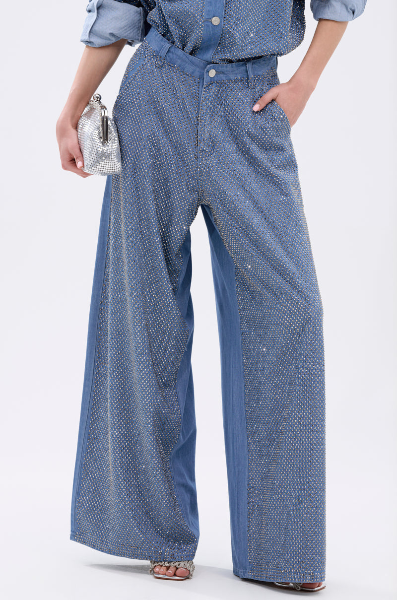 Wearing the BLING BLING DENIM RELAXED PANT with glittering rhinestones and a wide-leg fit, styled with a matching shirt, sparkly silver clutch, and open-toe heels for a high-rise denim look that shines.