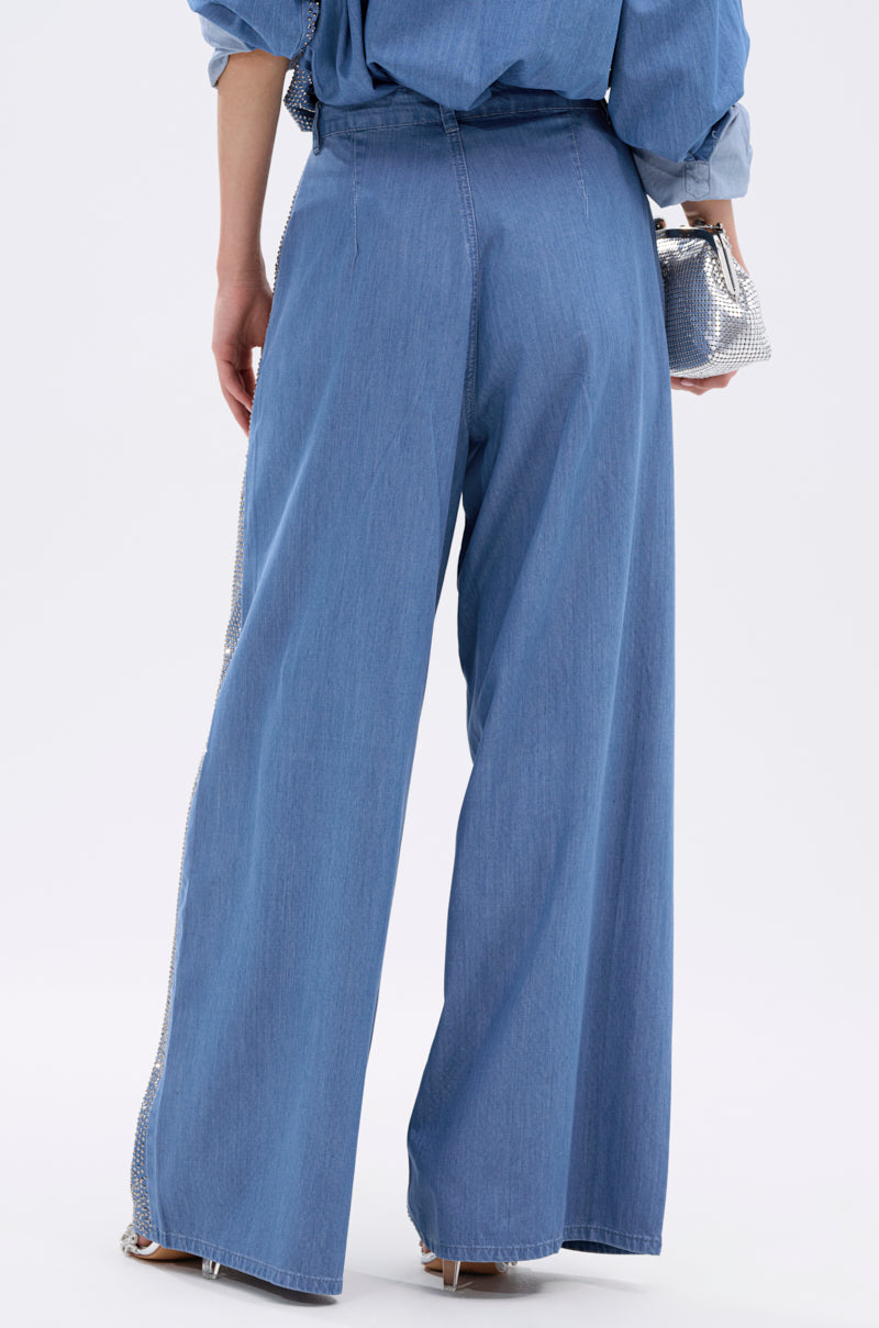 Seen from behind, a person wears the BLING BLING DENIM RELAXED PANT in light blue with a matching denim top, holding a small silver purse against a plain light background.