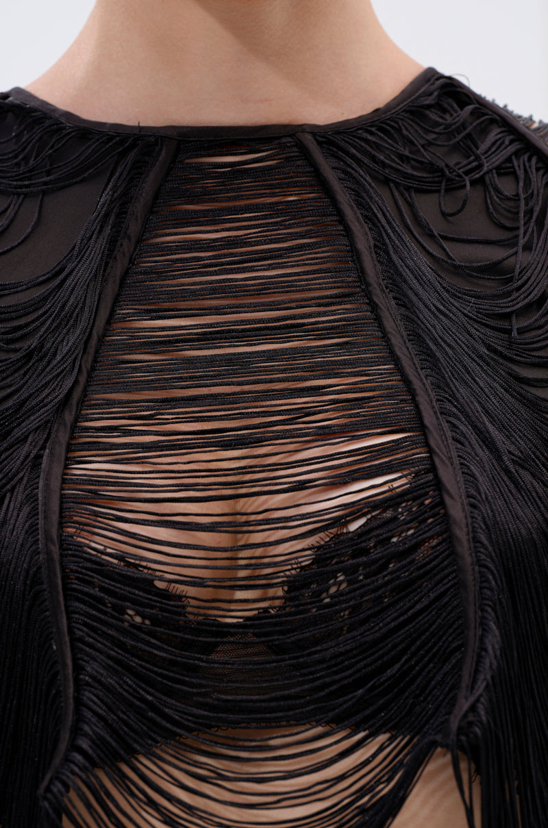 Close-up of a person wearing the LUCY FRINGE LONG SLEEVE BLOUSE, a black sheer top featuring layered fringe, striped semi-transparent fabric, and long sleeves, revealing a black lace bra underneath for a chic and textured look. 8