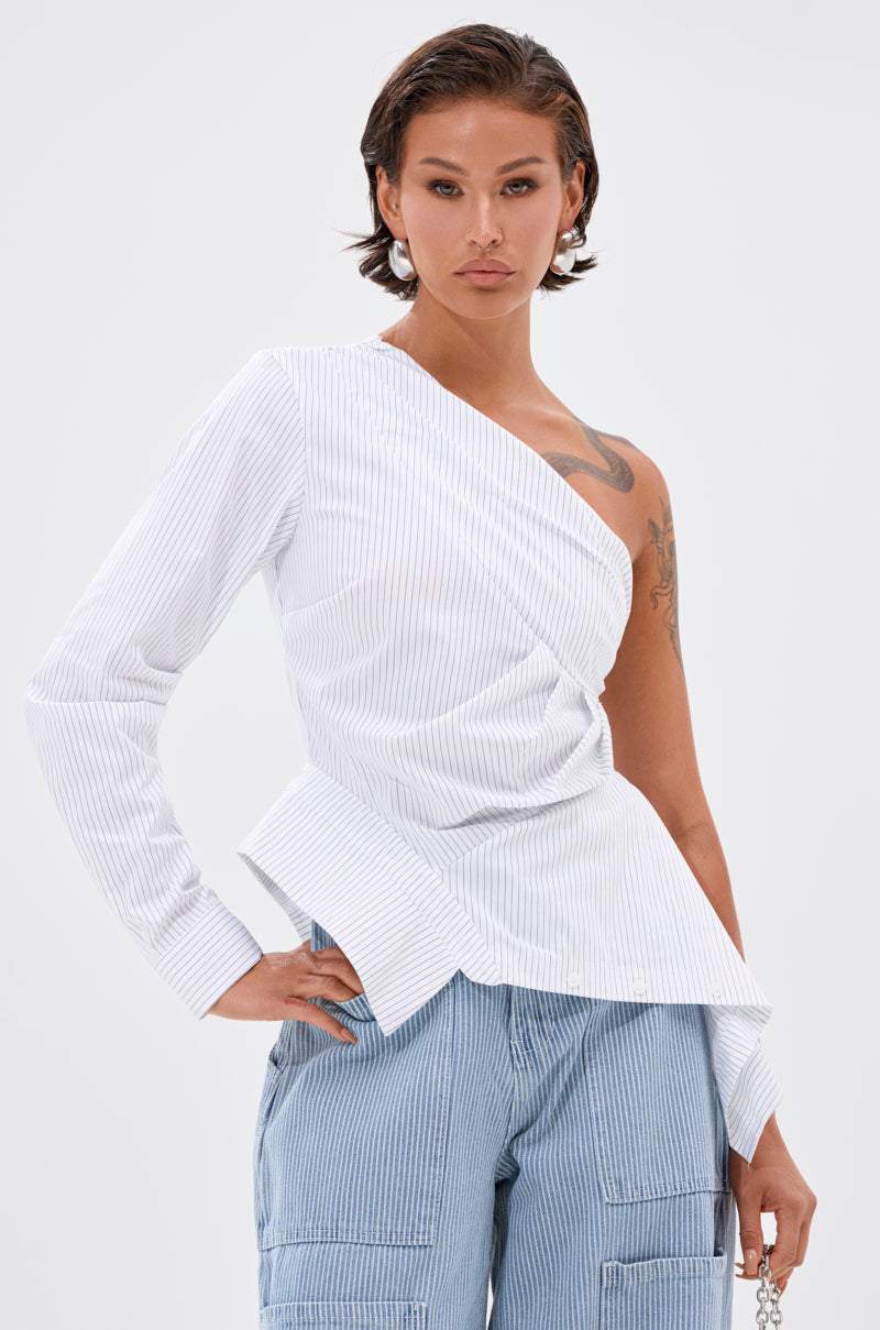 Wearing the ASSIA ONE SHOULDER BLOUSE, a white top with an asymmetrical neckline and pinstripe accents, paired with light blue pinstripe cargo pants, this individual stands confidently against a plain background.