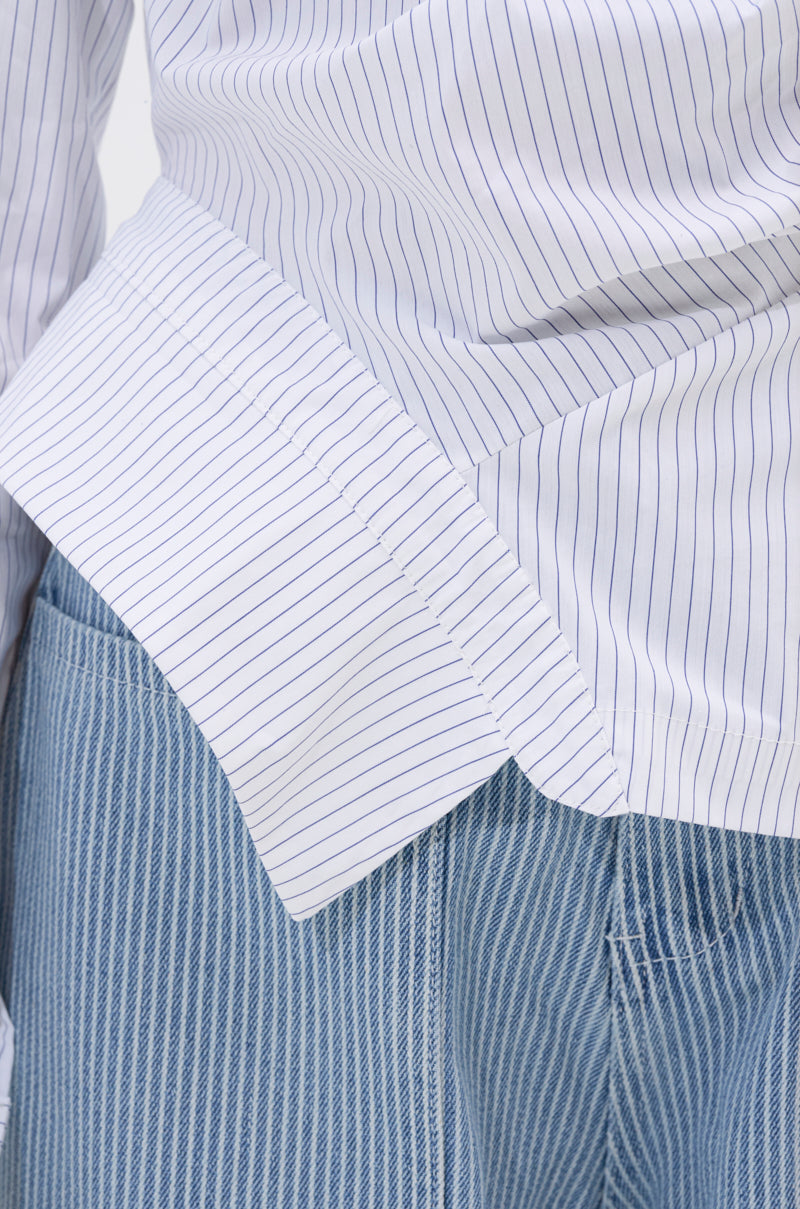 Close-up of a person wearing the ASSIA ONE SHOULDER BLOUSE with thin blue pinstripes and light blue denim jeans featuring thin white vertical stripes.