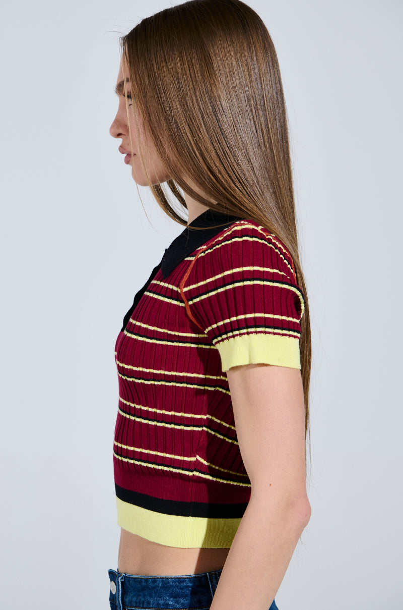 Sporting long straight hair, a person wears a ribbed knit School Girl Vibes Polo with red, black, and yellow stripes. Cropped and short-sleeved, the top pairs with classic blue jeans. They're in profile view, facing left. 2