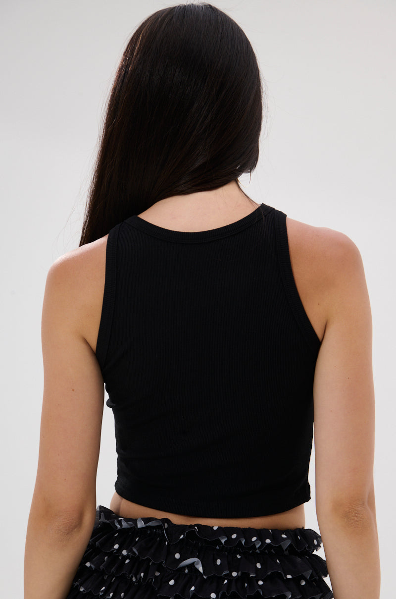 A woman with long, straight dark hair is shown from the back, wearing the KISSY FACE TANK TOP IN BLACK and a black skirt with white polka dots against a plain light background.