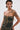 A woman with wet, slicked-back hair wears the DOWN AND DIRTY CAMO CORSET featuring yellow lace-up details and a curve-hugging fit, paired with a matching camo mini skirt. Tattoos on her shoulder and arm stand out against a plain background.