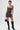 A tattooed woman confidently poses against a white background wearing the DOWN AND DIRTY CAMO CORSET, styled as a strapless, curve-hugging mini with lace-up details, paired with black knee-high boots and a small black handbag.