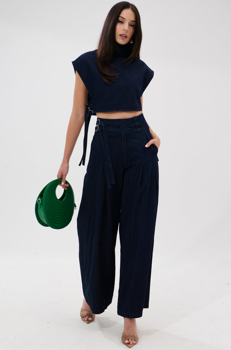 A woman with long dark hair stands against a white background wearing the YOU A REAL ONE DENIM BLOUSE and wide-leg pants, holding a round green handbag and wearing open-toe heels.