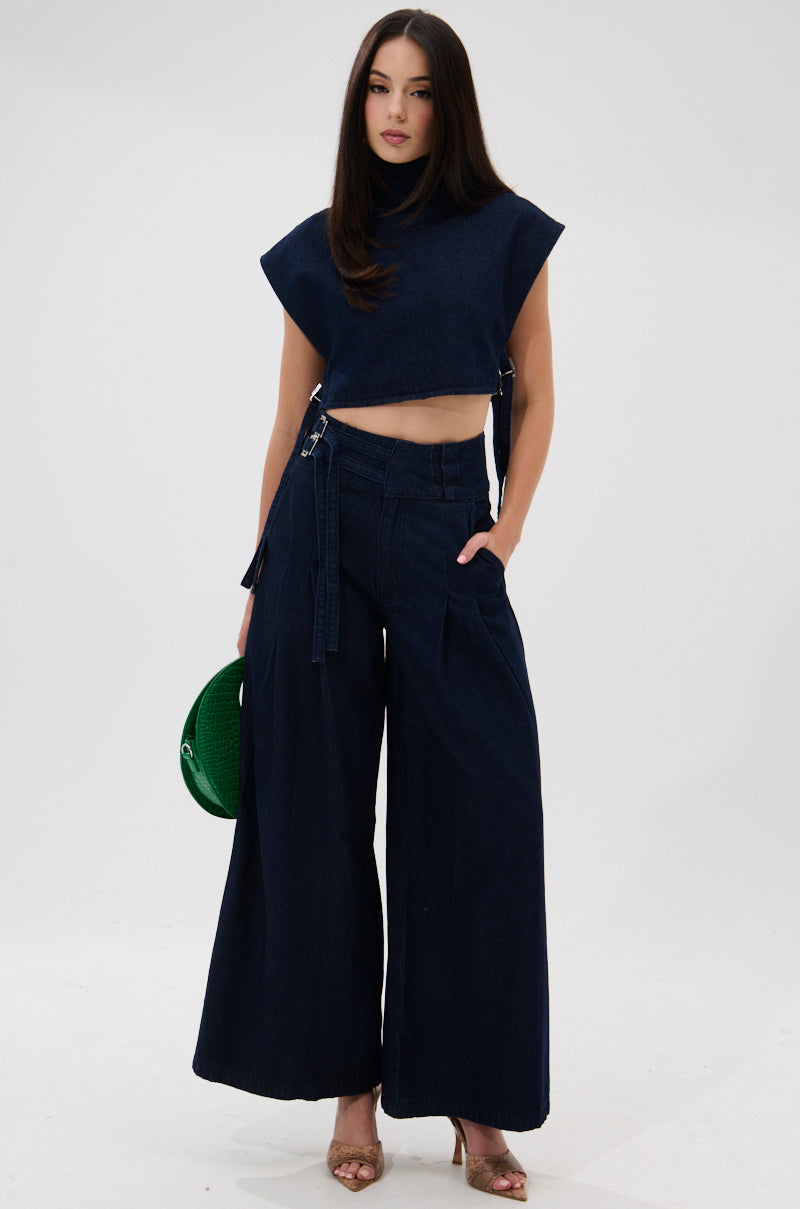 A woman stands against a white background wearing the YOU A REAL ONE DENIM BLOUSE, wide-leg pants, gold open-toe heels, and holding a green handbag.