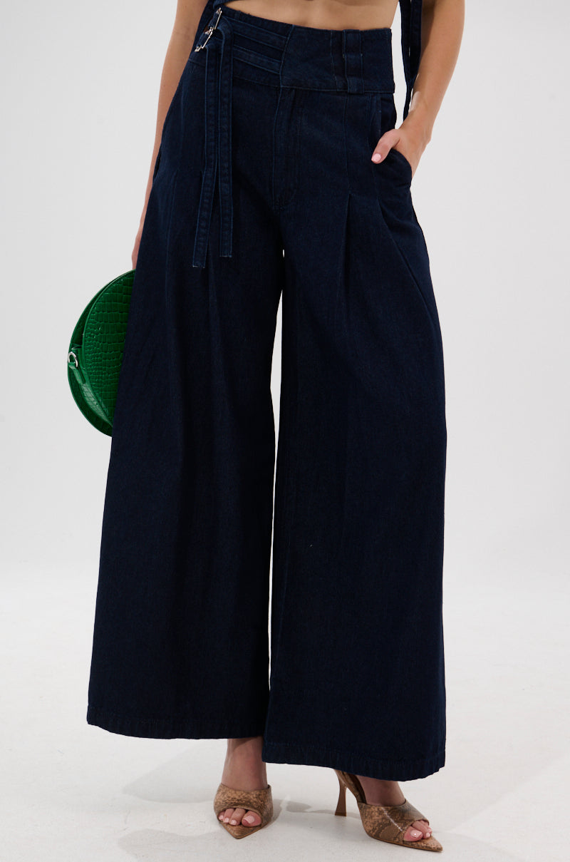 Wearing YOU A REAL ONE DENIM TROUSER—high-rise, wide-leg jeans with a denim double buckle belt—paired with tan open-toe heels and a round green handbag, shown from the shoulders down.