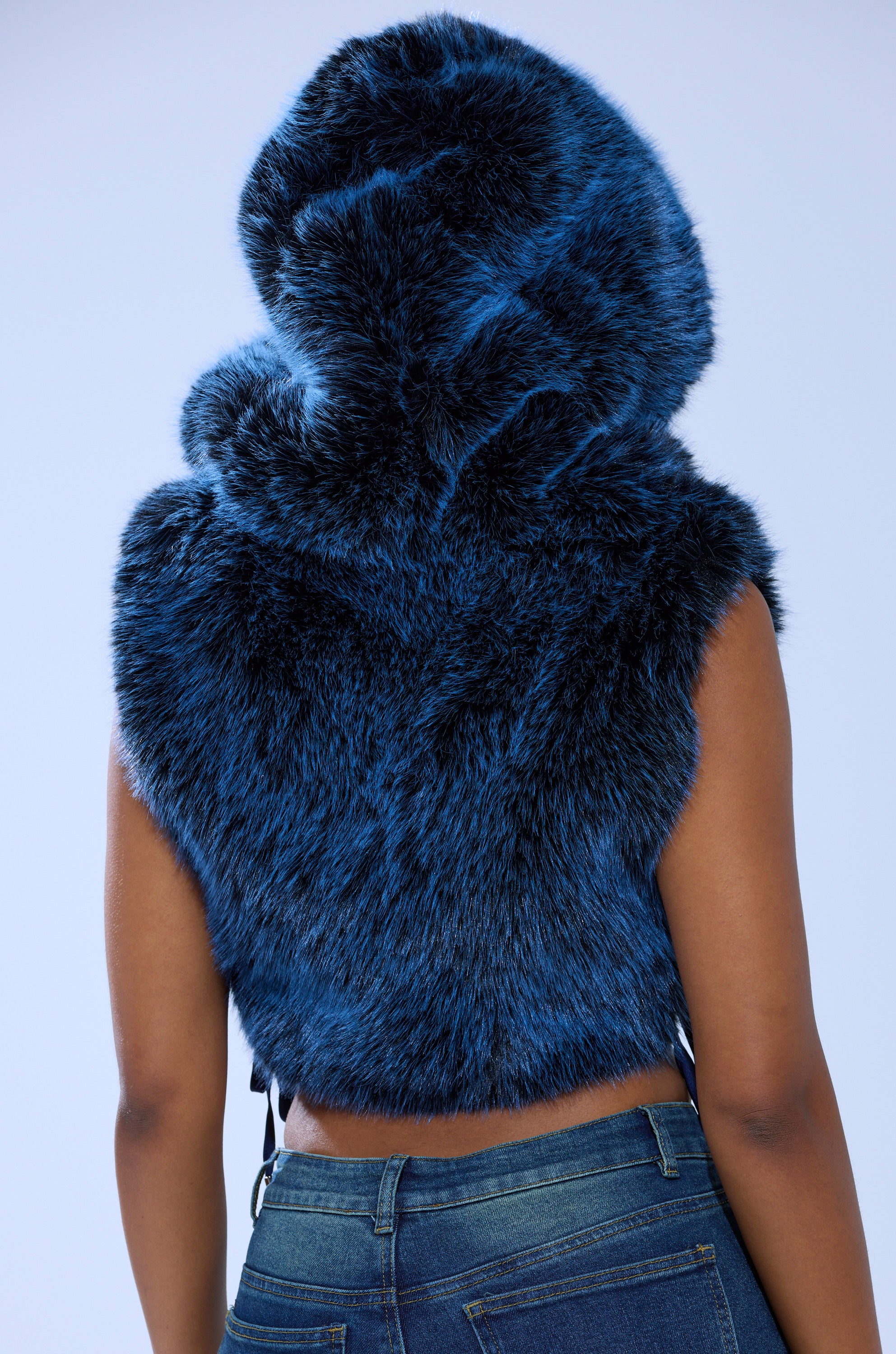 A person seen from the back wears the ALL A DREAM FUR TOP, a sleeveless, dark blue faux fur hoodie with plush Y2K-inspired texture, paired stylishly with blue denim jeans.