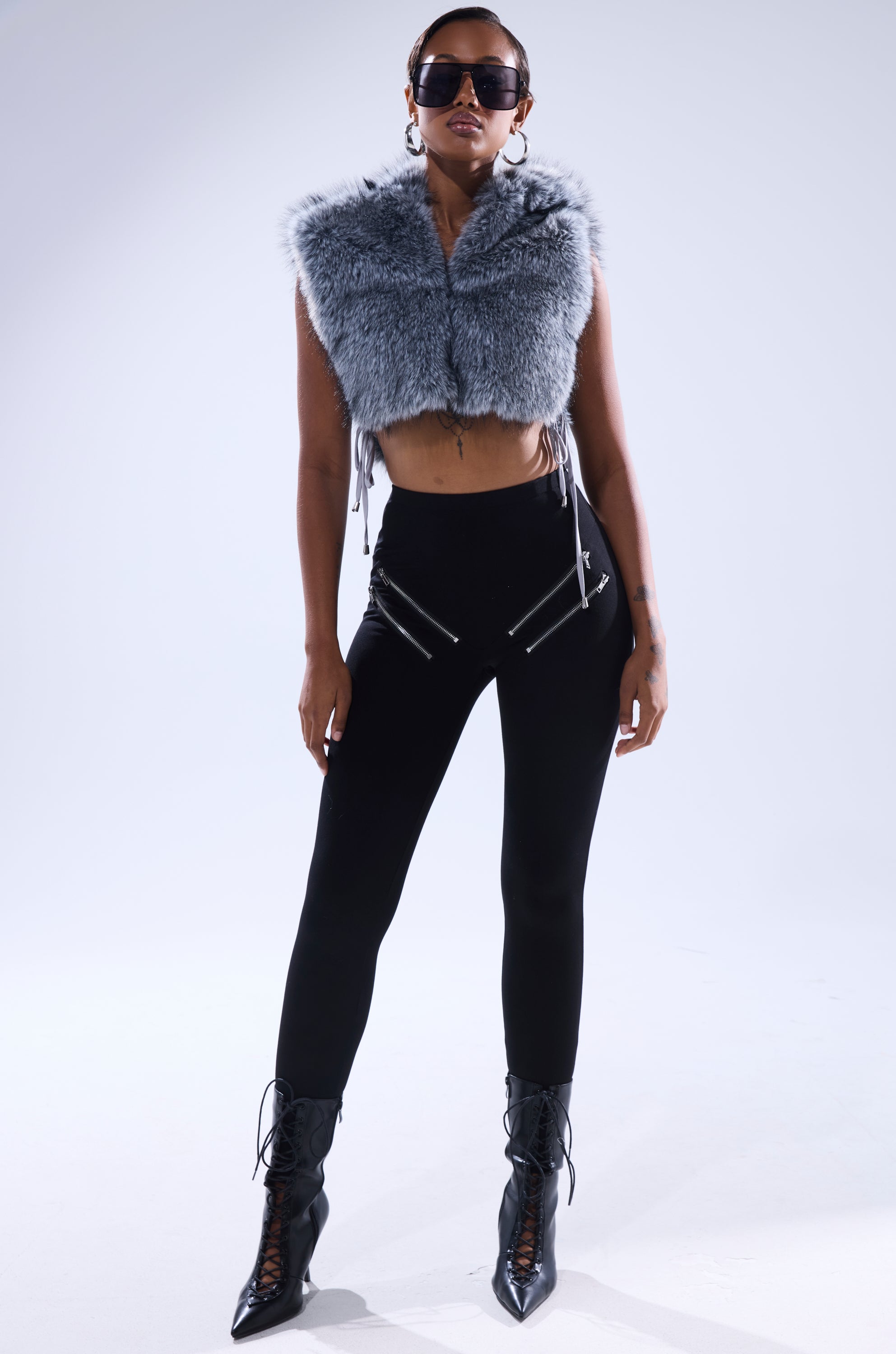 A woman stands confidently in black sunglasses, the TOUCH ME FUR TOP styled as a gray cropped vest, high-waisted black zippered pants, and black lace-up ankle boots against a plain light background. 8