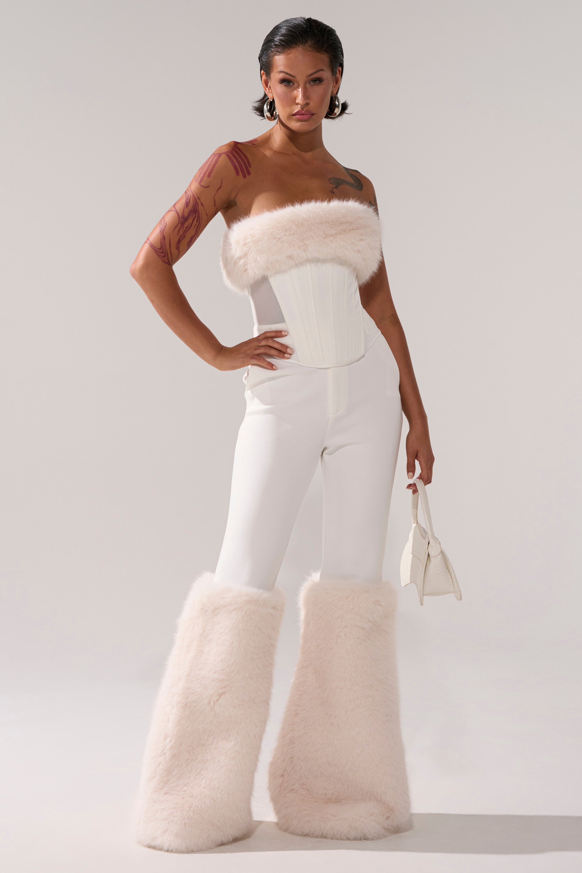 A woman in a white outfit exudes elegance in her SNOW BUNNY TROUSER WITH FUR CUFF, perfect for a crisp, stylish look.