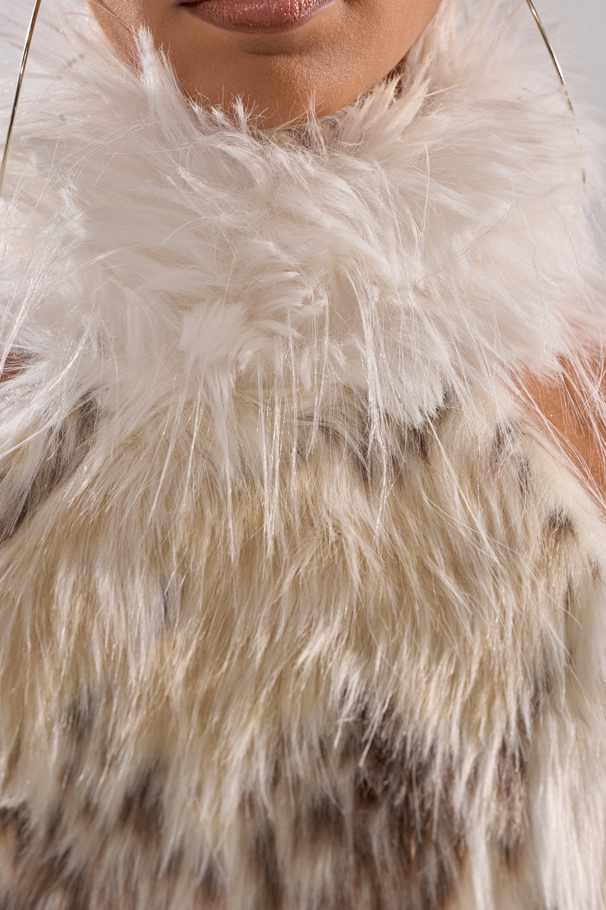A close-up of a person wearing the FLINTSTONES MOCK NECK FUR TOP, a fluffy white and beige faux fur piece, with large gold hoop earrings visible and only the lower half of their face shown.